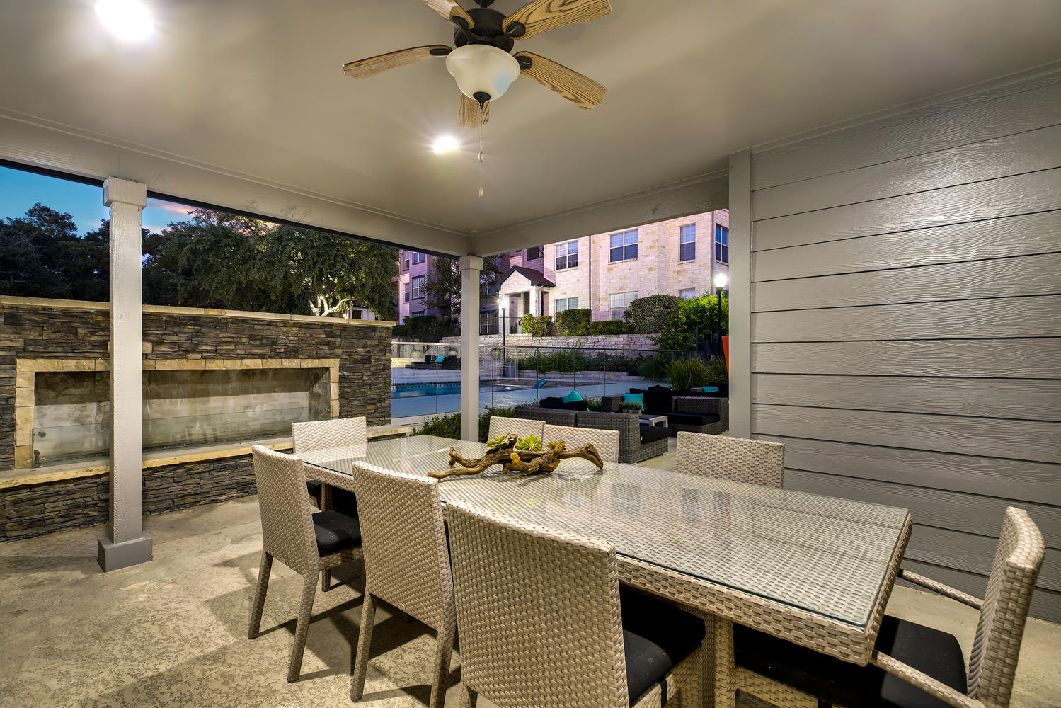 Night time shot of a covered outdoor dining table in front of an elegant fireplace