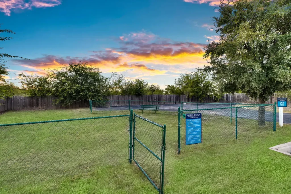 Fenced, grassy dog park with bench and signage