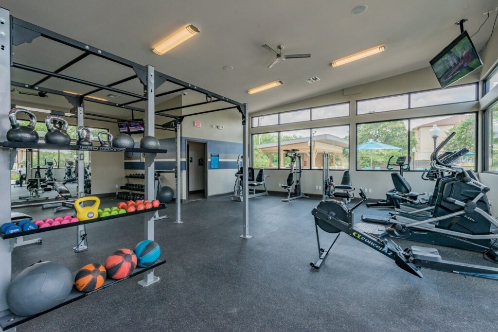 24-hour gym with weights and medicine balls, ceiling fan, large windows, and lots of equipment