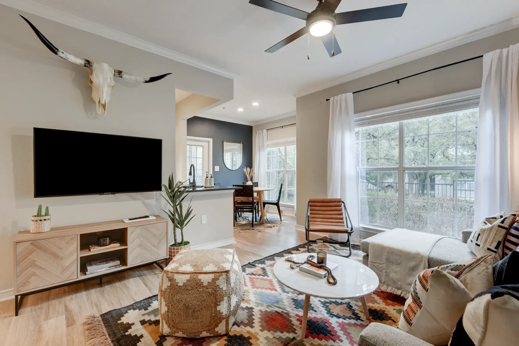 Living room near the kitchen with a ceiling fan, wood-style flooring, and a window